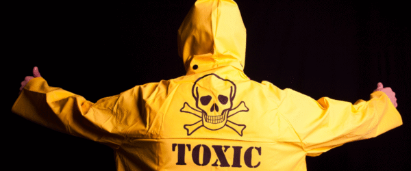 Human with a yellow jacket on and word toxic with the skull and cross bones symbol emblazoned on the back