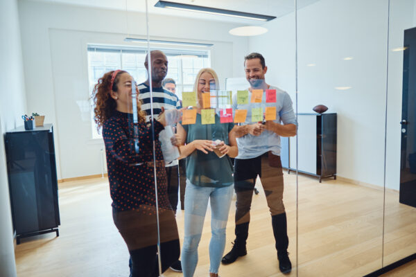 Image of people brainstorming using post it notes in an office where people are smiling, one person is holding coffee they could be the manager.